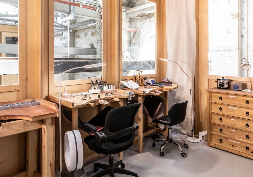 A light, glass-fronted studio overlooking an industrial warehouse space with light wood structure and fittings and two desk chairs.